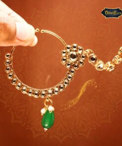 Close-up of a Zehra Emerald Droplet Nath, a gold-plated nose ring with a crescent silhouette and a striking emerald-green droplet, against a soft background.